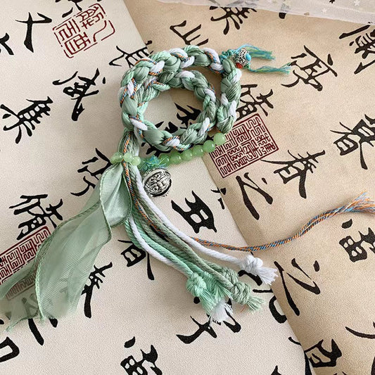 Mountain Ghost - Emerald Bloom Bracelet with green hues and tassels on decorative paper.