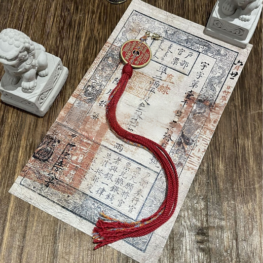 Mountain Ghost - Crimson Guardian Tassel Charm with red tassel and Chinese coin on decorative background.