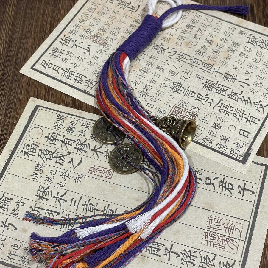 Mountain Ghost Golden Fortune Bell Charm with multicolored threads and Chinese coins on a wooden surface.