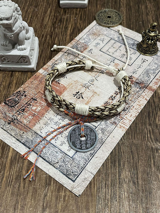 Mountain Ghost Mystic Wealth Bracelet with Taoist symbols and braided cord on wooden surface.